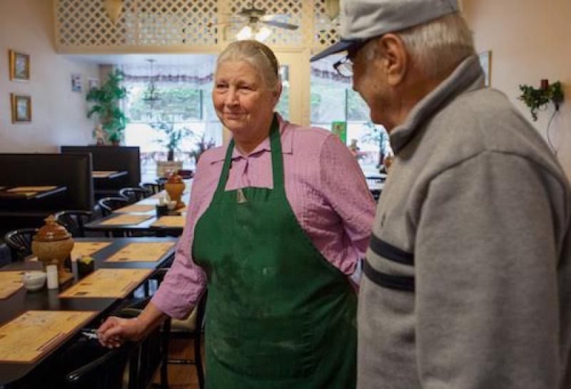 lady Woman in pink shirt with green apron speaking with a man in a restaurant