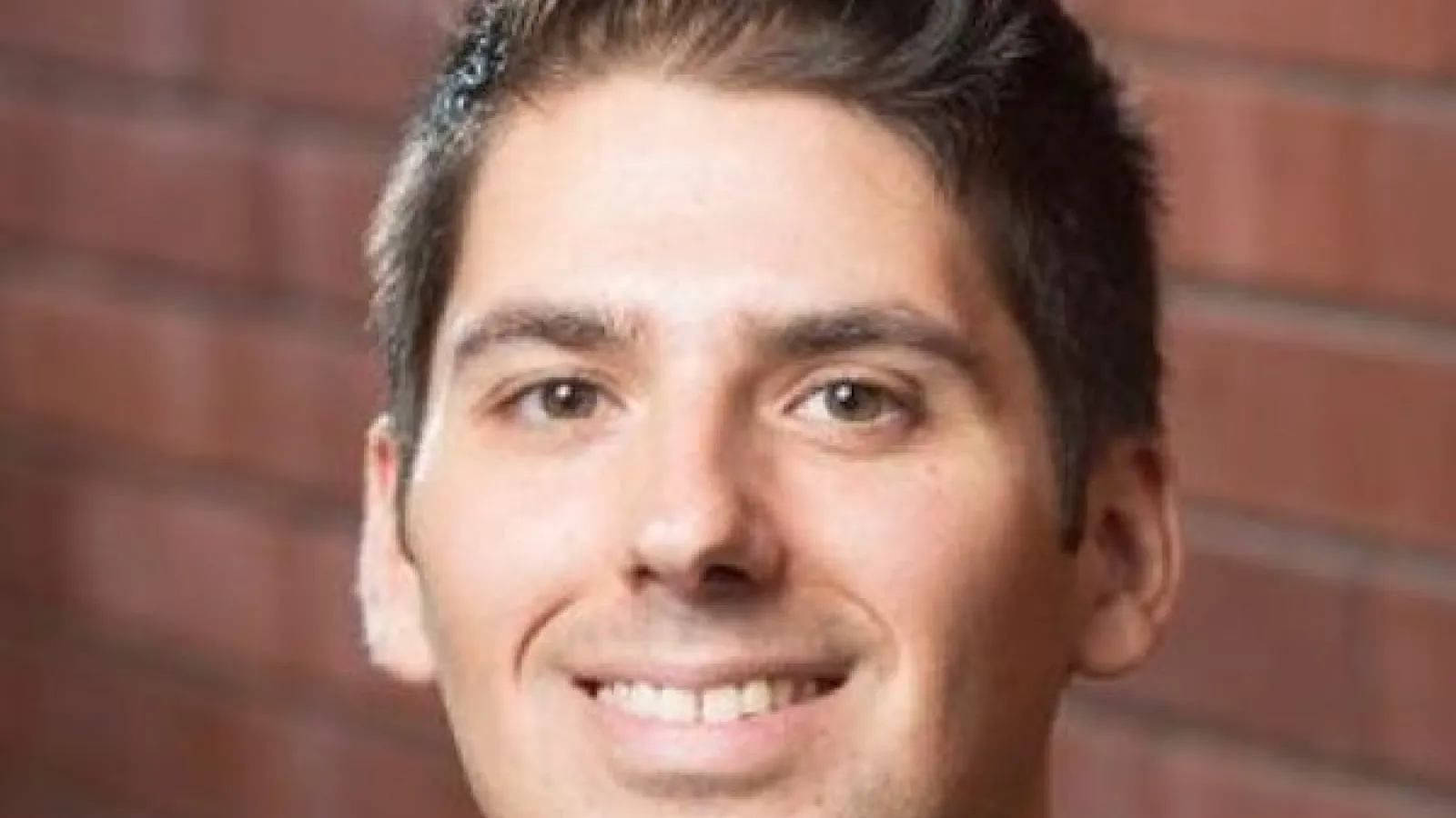 Color headshot image of Alexander Rocklin who has light skin and shot brown hair. A blurred brick wall can be seen in the background.