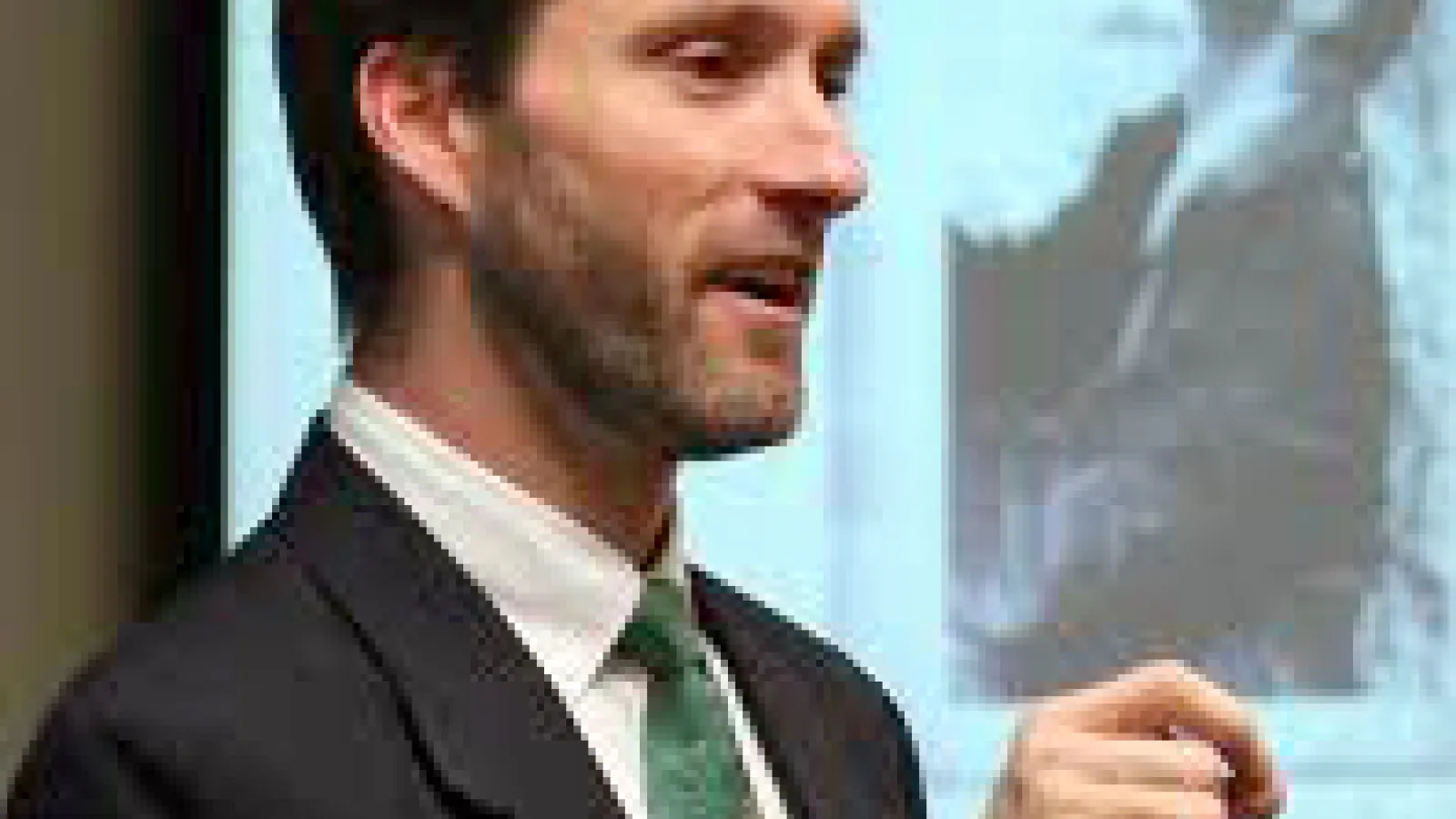 Color image of Dr. Gregory Htizhusen lecturing and gesturing in front of a blurred presentation screen.
