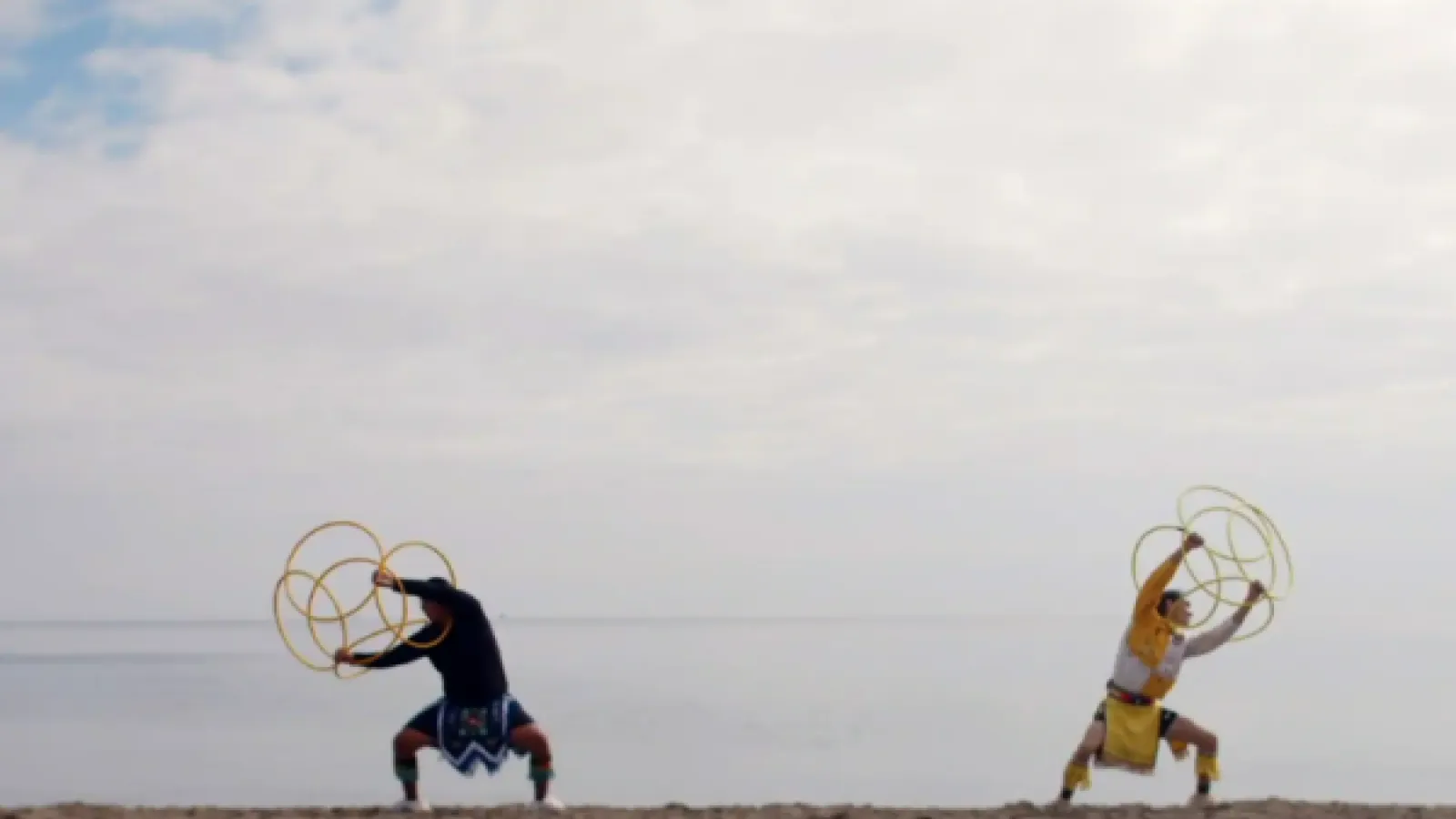 Two people on a beach with a big sky holding hula hoops