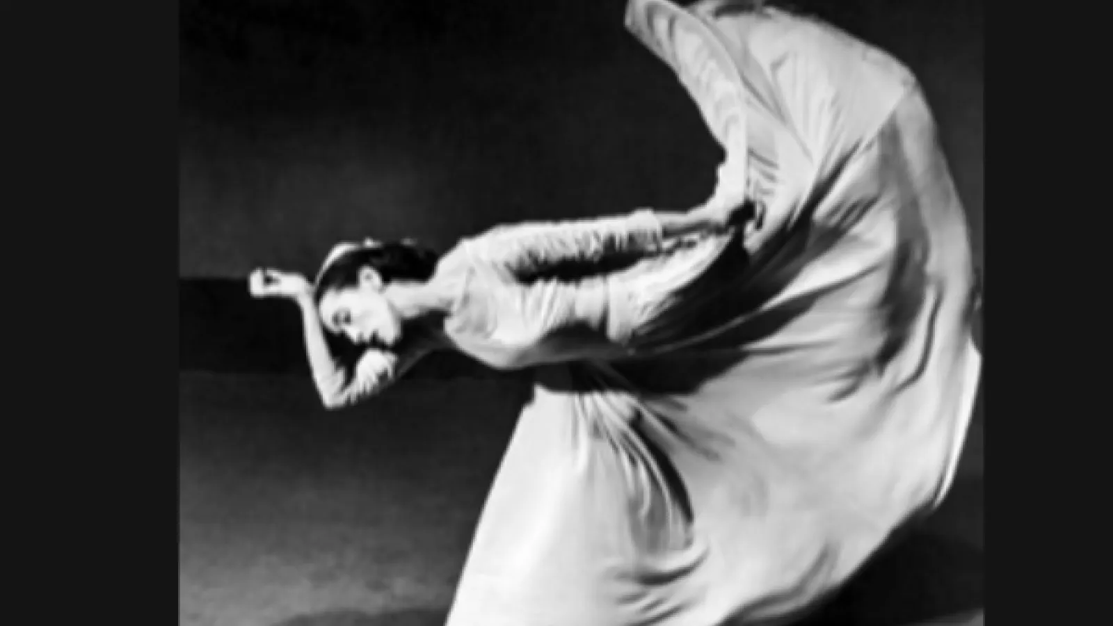 A black and white photo of a woman with a long full skirt with her foot above her head