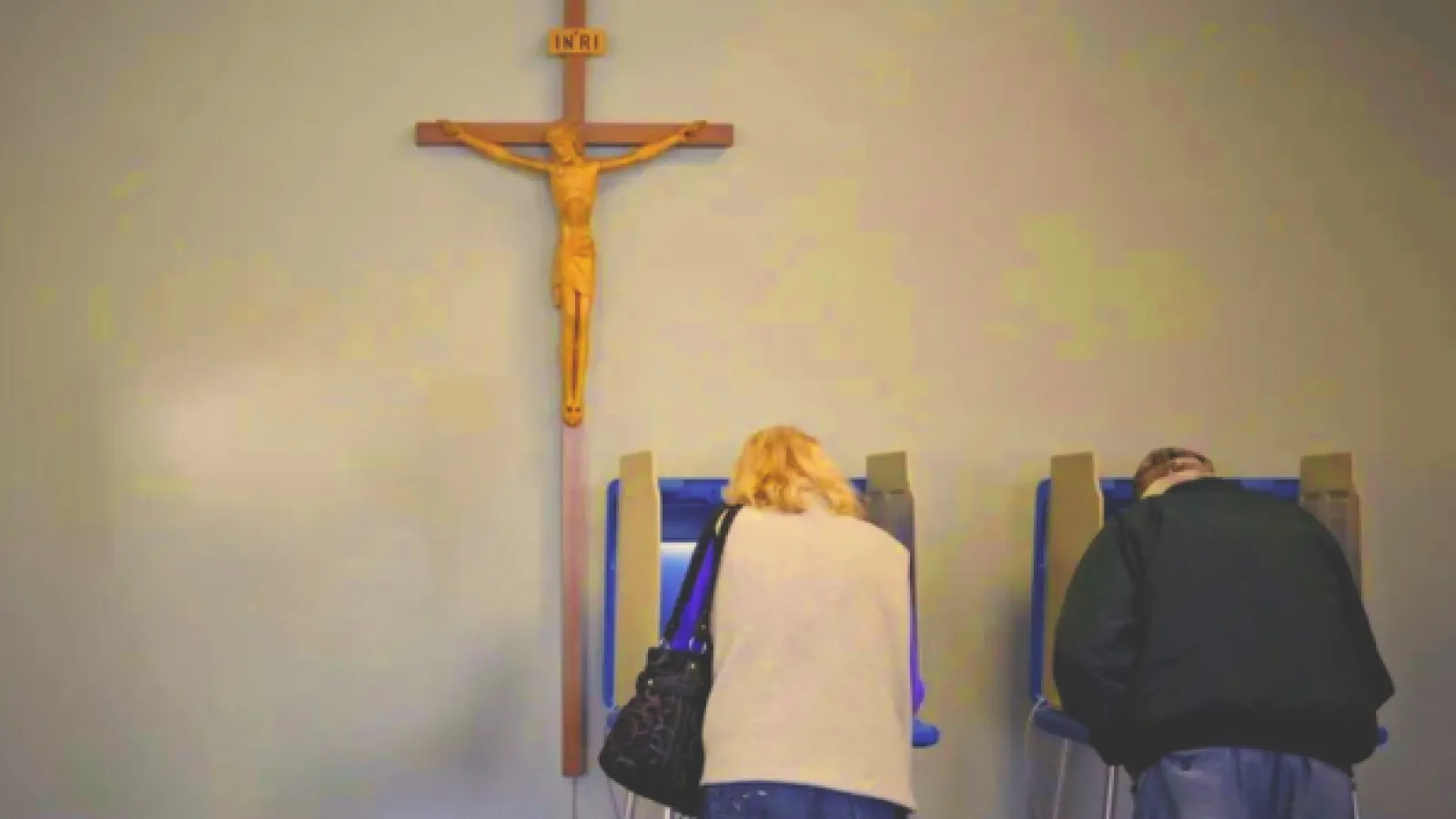 Two people at voting machines with a crucifix hanging above them