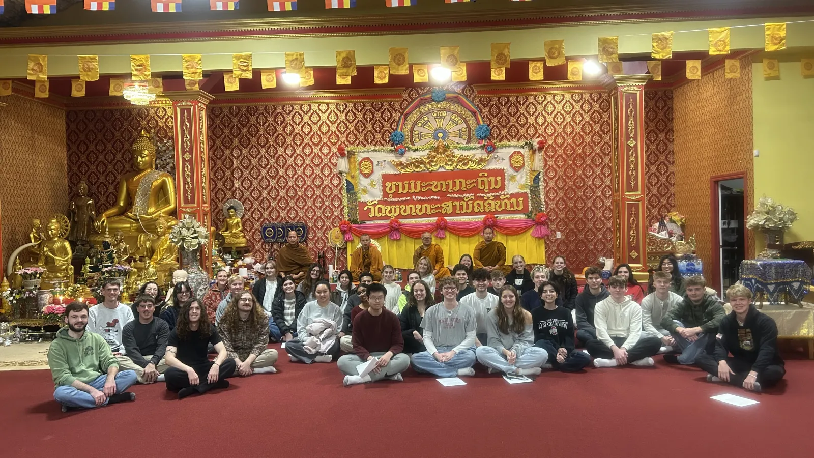Students sitting on the ground in front of four Buddhist Monks