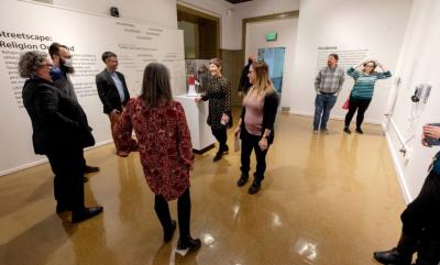 12 people standing in a gallery space with big posters on white walls. 