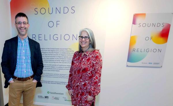 Isaac Weiner and Amy DeRogatis standing in front of the curator's statement on the wall in a gallery poster exhibition