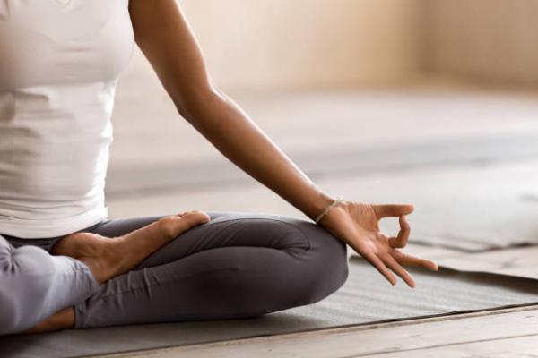 Color image of torso, legs, and hand of a body in a seated position where the index finger and thumb are touching in a "ok" gesture, suggestive of meditative practice