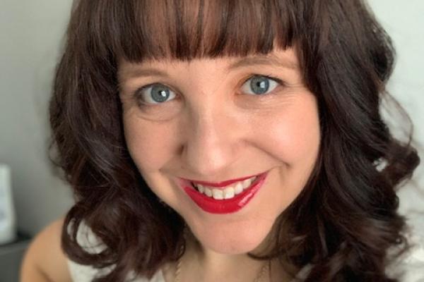 a headshot of a woman with medium length brown hair, blue eyes, and bright red lipstick smiling