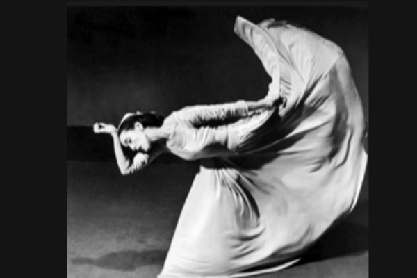 A black and white photo of a woman with a long full skirt with her foot above her head