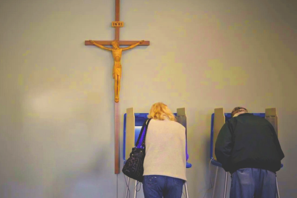 Two people at voting machines with a crucifix hanging above them