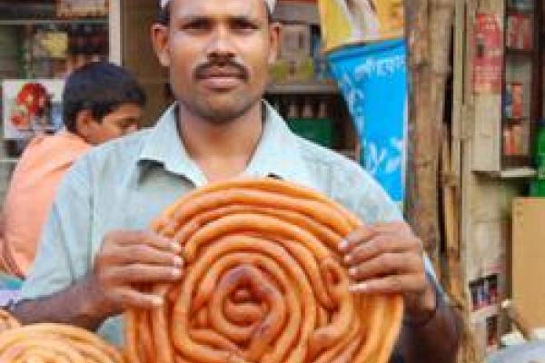 A man holding a large round loaf of bread that looks like a snail shell with a thin spiral 